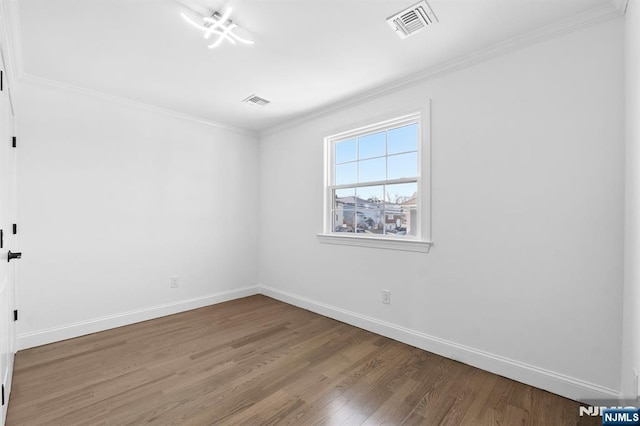 empty room featuring crown molding, wood finished floors, visible vents, and baseboards