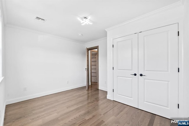 unfurnished bedroom featuring light wood-type flooring, visible vents, a closet, crown molding, and baseboards