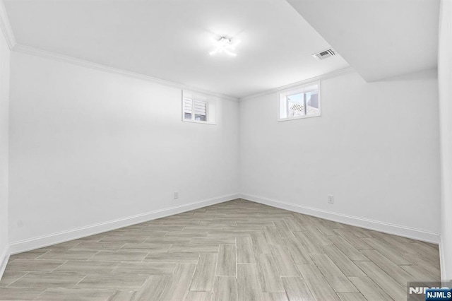 below grade area featuring light wood-style floors, visible vents, crown molding, and baseboards