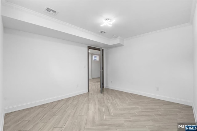 empty room with visible vents, light wood-type flooring, crown molding, and baseboards