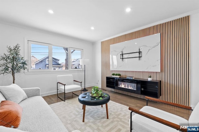 living room with ornamental molding, a glass covered fireplace, wood finished floors, recessed lighting, and baseboards