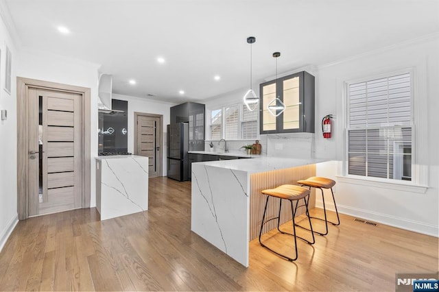 kitchen featuring visible vents, a kitchen bar, ornamental molding, a peninsula, and freestanding refrigerator