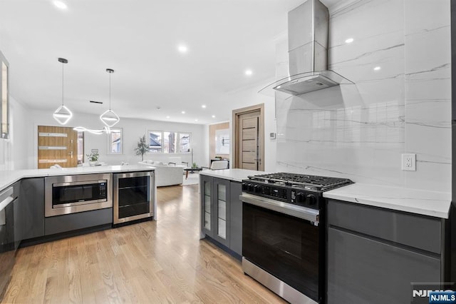 kitchen with gray cabinetry, stainless steel microwave, gas stove, wine cooler, and wall chimney range hood