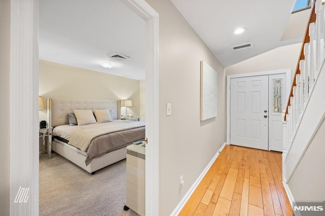 hallway with baseboards, visible vents, light wood-style flooring, stairs, and vaulted ceiling