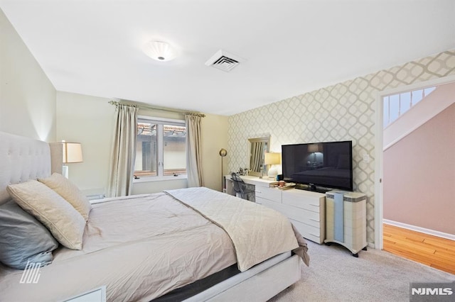 bedroom with visible vents, light carpet, wallpapered walls, baseboards, and an accent wall