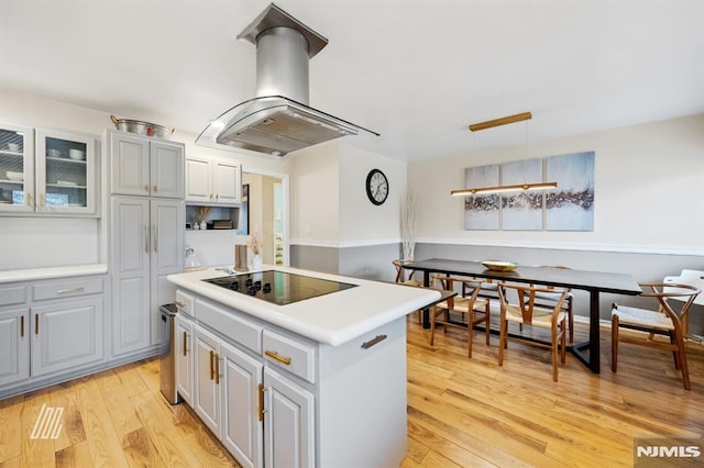 kitchen featuring a kitchen island, light countertops, light wood-type flooring, island range hood, and black electric cooktop