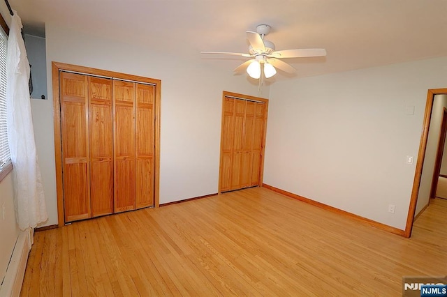 unfurnished bedroom with a ceiling fan, baseboards, a baseboard radiator, light wood-style flooring, and two closets