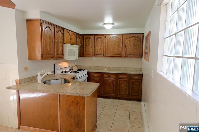 kitchen featuring light tile patterned floors, brown cabinets, a peninsula, white appliances, and a sink