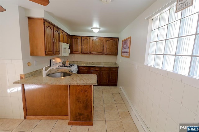 kitchen featuring a sink, white appliances, tile walls, brown cabinetry, and light tile patterned floors