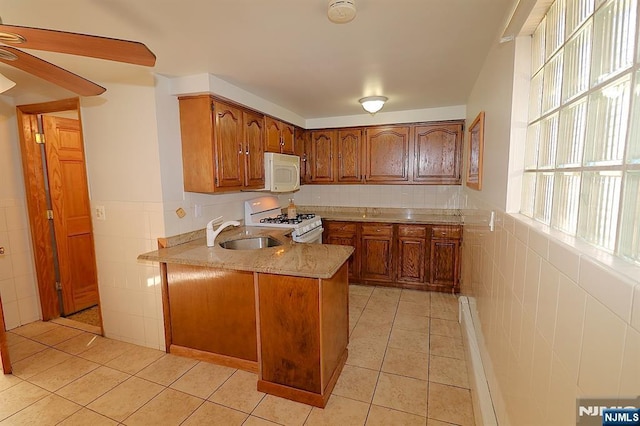 kitchen with white appliances, light tile patterned floors, brown cabinetry, a peninsula, and a sink