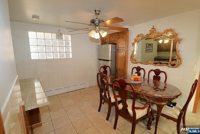 dining room with light tile patterned floors, a baseboard heating unit, tile walls, and a wainscoted wall