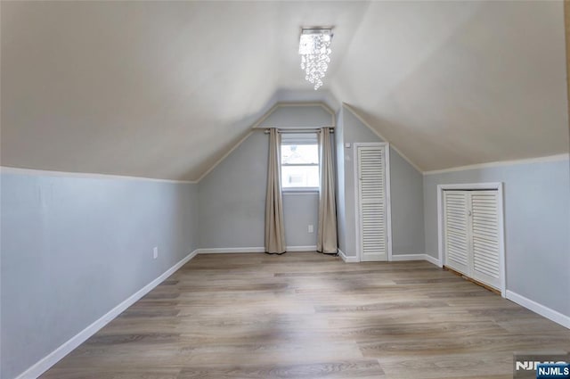 bonus room with baseboards, lofted ceiling, an inviting chandelier, and wood finished floors