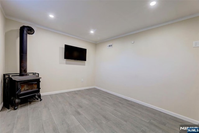 living area with baseboards, light wood-type flooring, ornamental molding, recessed lighting, and a wood stove