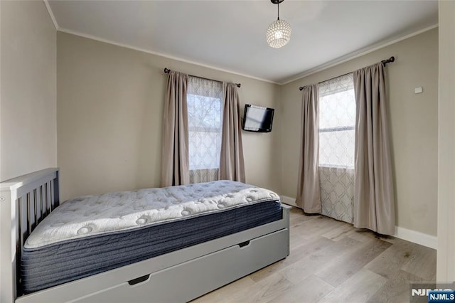 bedroom featuring baseboards, multiple windows, crown molding, and light wood finished floors