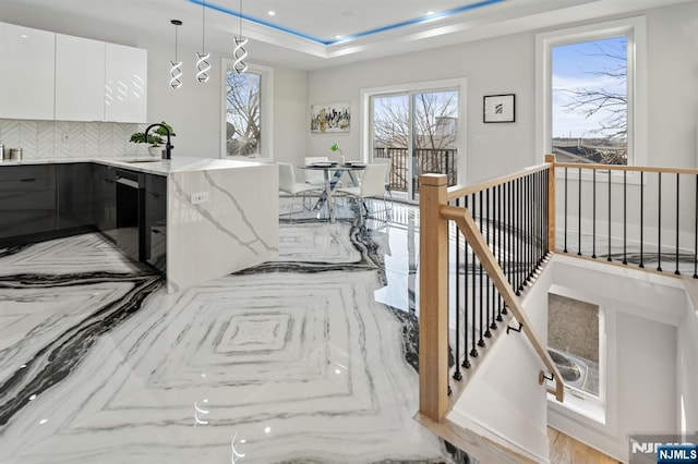 interior space with a peninsula, a sink, white cabinetry, a raised ceiling, and backsplash