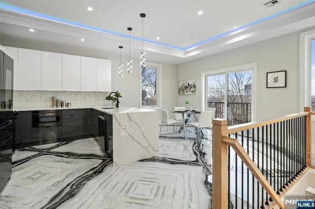 kitchen featuring modern cabinets, a sink, a tray ceiling, wall oven, and a peninsula