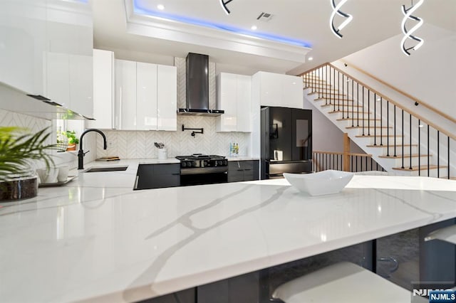 kitchen featuring tasteful backsplash, a peninsula, black appliances, wall chimney exhaust hood, and a sink