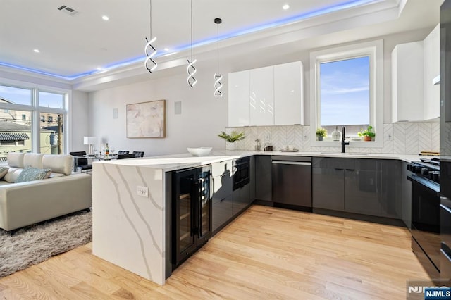 kitchen featuring visible vents, a peninsula, light wood-style floors, black range with gas cooktop, and stainless steel dishwasher