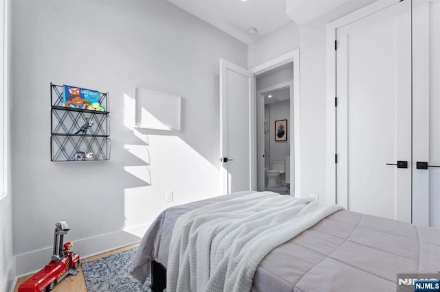 bedroom featuring baseboards, wood finished floors, and ensuite bathroom