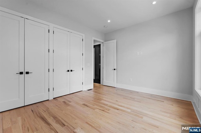 unfurnished bedroom featuring recessed lighting, light wood-style floors, baseboards, and two closets