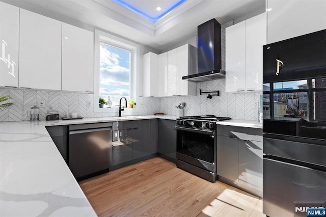 kitchen featuring gas stove, a sink, stainless steel dishwasher, wall chimney range hood, and modern cabinets