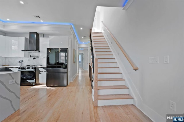 kitchen featuring visible vents, wall chimney range hood, smart refrigerator, gas stove, and white cabinetry