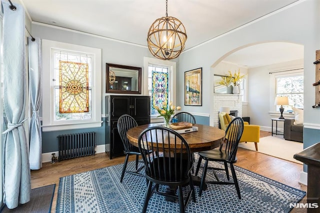 dining area featuring wood finished floors, arched walkways, radiator, crown molding, and a brick fireplace