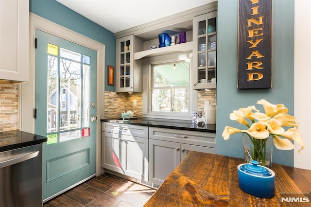 kitchen with wood counters, backsplash, stainless steel dishwasher, glass insert cabinets, and wood tiled floor