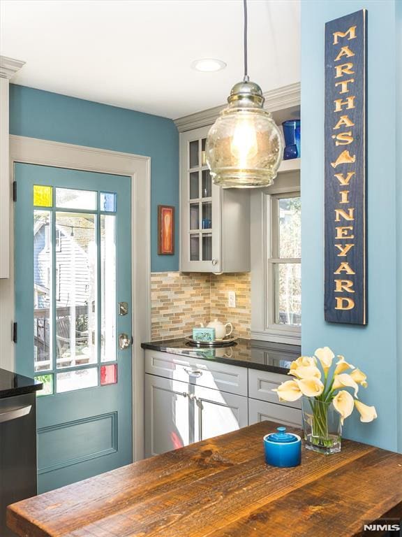 kitchen featuring pendant lighting, wood counters, backsplash, glass insert cabinets, and dishwasher