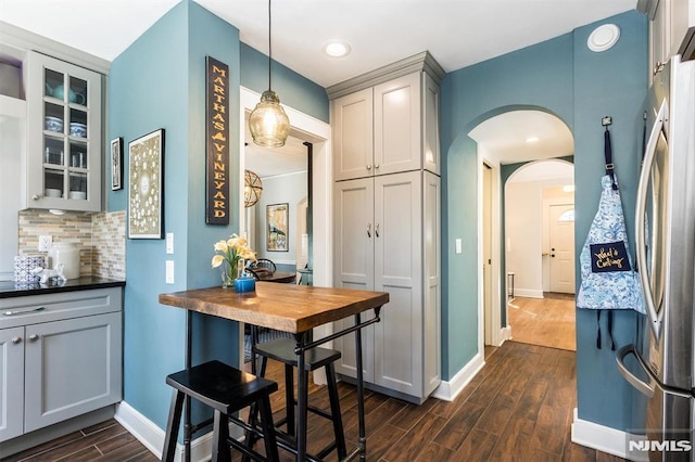 kitchen with tasteful backsplash, glass insert cabinets, baseboards, dark wood-style floors, and arched walkways