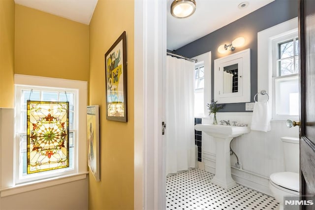 full bath featuring a wainscoted wall, toilet, plenty of natural light, and a sink