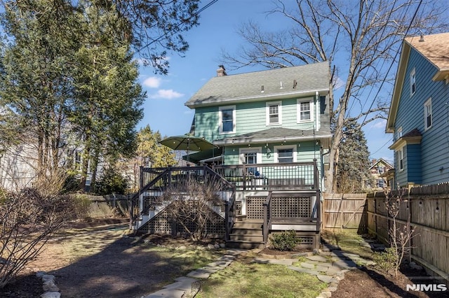 rear view of house with stairway, a fenced backyard, a shingled roof, a chimney, and a deck