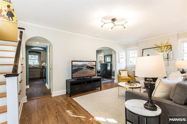 living area with arched walkways, stairway, dark wood finished floors, and ornamental molding