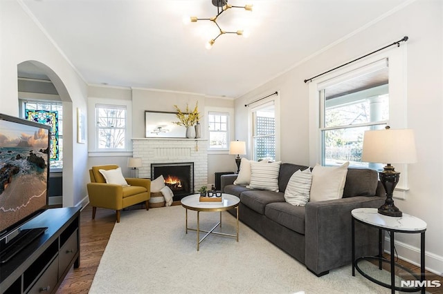 living room with baseboards, ornamental molding, a fireplace, wood finished floors, and arched walkways