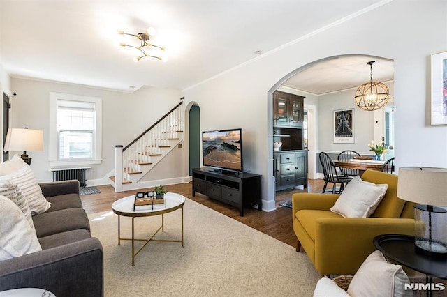 living area with ornamental molding, wood finished floors, radiator heating unit, stairway, and an inviting chandelier