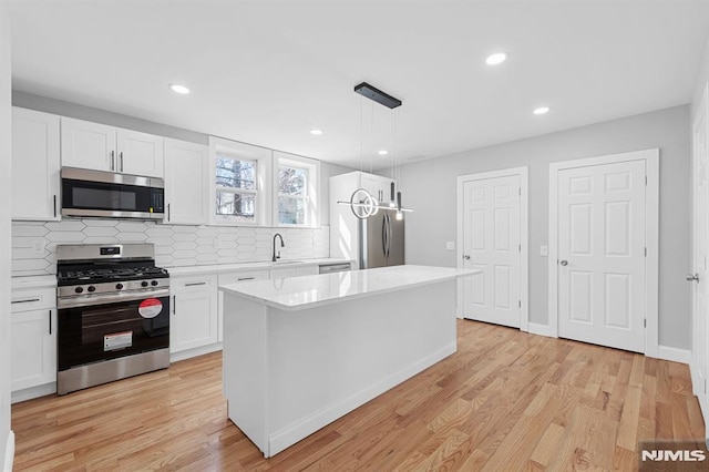 kitchen with light countertops, light wood-style floors, appliances with stainless steel finishes, white cabinetry, and tasteful backsplash