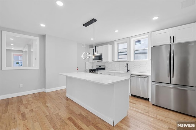 kitchen with a sink, a kitchen island, white cabinetry, stainless steel appliances, and light wood finished floors