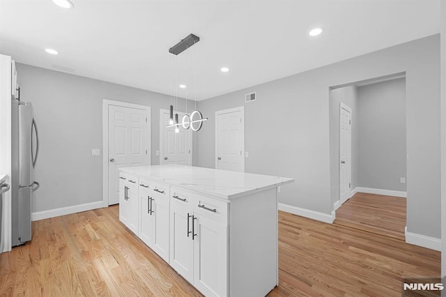 kitchen featuring light stone countertops, visible vents, freestanding refrigerator, and light wood-type flooring