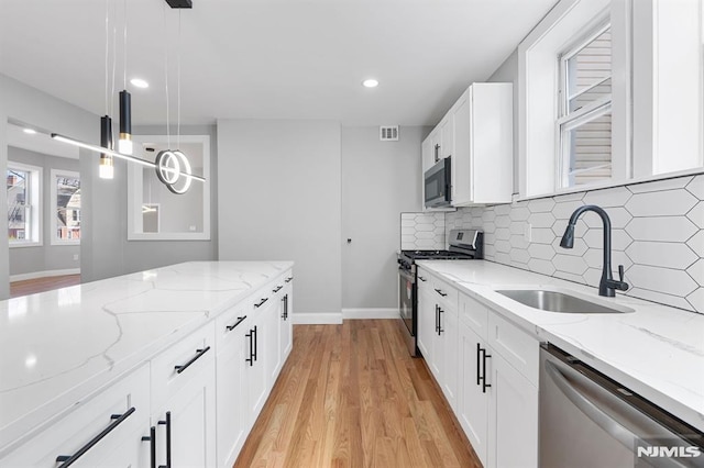 kitchen featuring backsplash, appliances with stainless steel finishes, light wood-style floors, white cabinetry, and a sink