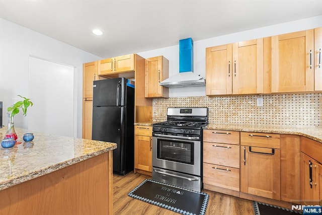 kitchen with gas range, light wood-type flooring, decorative backsplash, freestanding refrigerator, and wall chimney exhaust hood