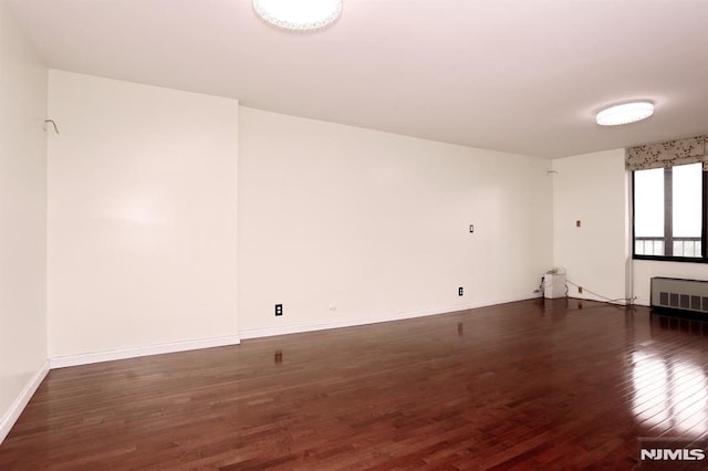 spare room with baseboards, wood finished floors, and radiator heating unit