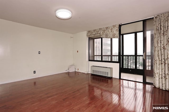 empty room featuring radiator, wood finished floors, and baseboards