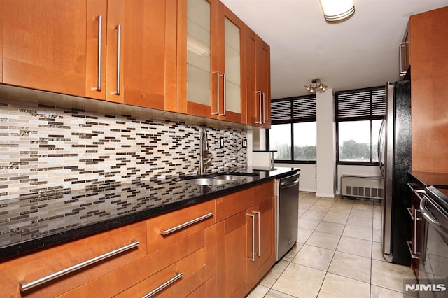 kitchen featuring light tile patterned floors, a sink, decorative backsplash, glass insert cabinets, and appliances with stainless steel finishes