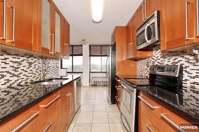 kitchen featuring backsplash, dark stone counters, appliances with stainless steel finishes, brown cabinetry, and a sink