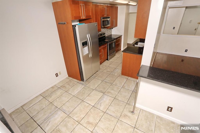 kitchen with light tile patterned floors, baseboards, decorative backsplash, appliances with stainless steel finishes, and brown cabinets