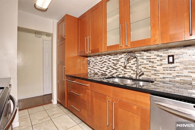 kitchen with brown cabinetry, a sink, dark stone counters, and stainless steel dishwasher