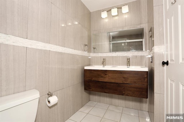 bathroom featuring toilet, a shower, tile walls, tile patterned flooring, and double vanity