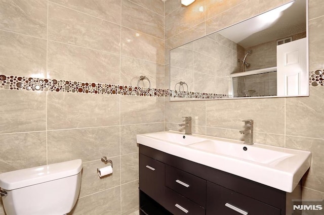 bathroom featuring toilet, tasteful backsplash, tile walls, tiled shower, and vanity