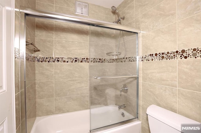 full bath with visible vents, toilet, and shower / bath combination with glass door