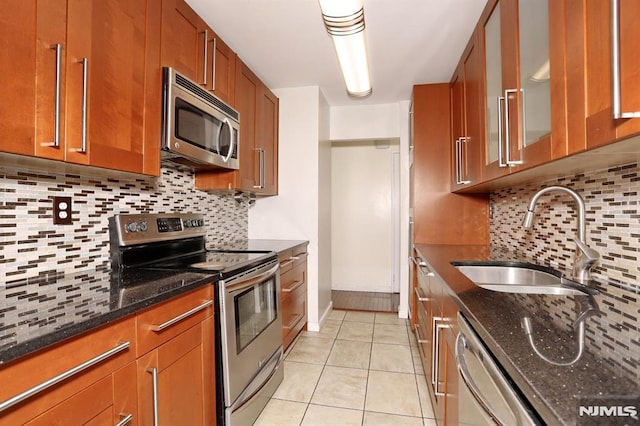 kitchen featuring dark stone countertops, light tile patterned floors, brown cabinetry, a sink, and appliances with stainless steel finishes